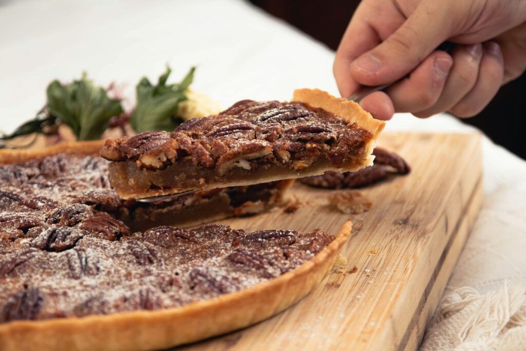 Close-up of a homemade pecan pie slice being removed on a wooden board.
